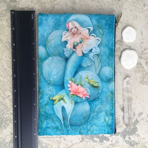 May include: A blue zippered pouch featuring a watercolour illustration of a mermaid with long white hair, surrounded by bubbles and sea turtles. The pouch has the text "FOREVERFAIRY.ETSY.COM" printed on the bottom.