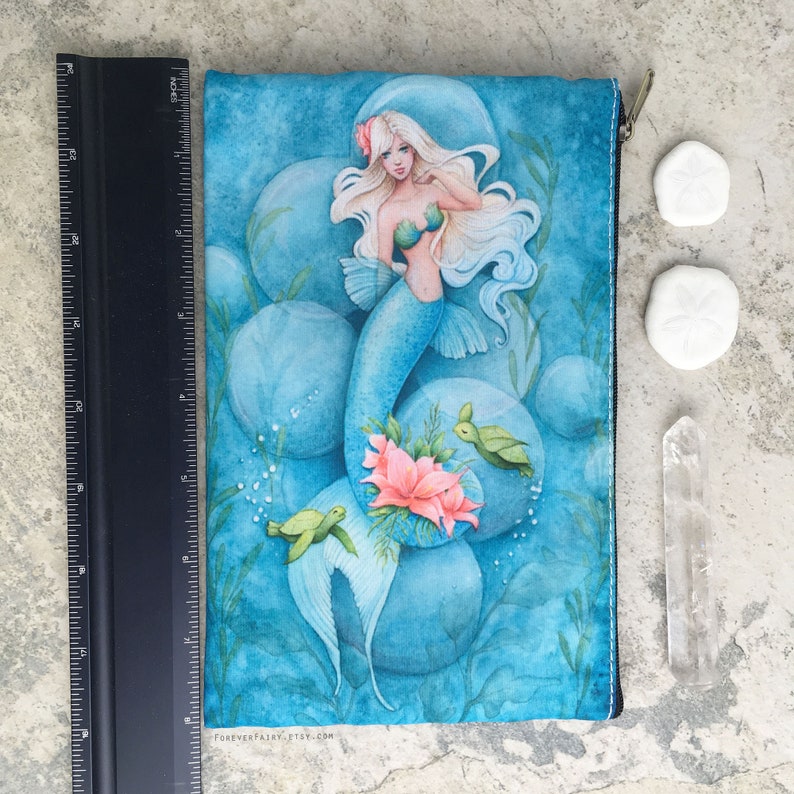 May include: A blue zippered pouch featuring a watercolour illustration of a mermaid with long white hair, surrounded by bubbles and sea turtles. The pouch has the text "FOREVERFAIRY.ETSY.COM" printed on the bottom.