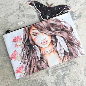 May include: A white zippered pouch with a colorful illustration of a woman with long brown hair, wearing a beaded necklace and feathers. The woman has a white face with red and white paint markings. The background is white with pink flowers.