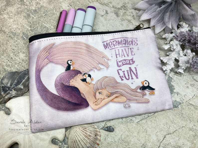 May include: A white zippered pouch with a purple mermaid and the text "Mermaids Have More Fun". The mermaid is surrounded by three small black and white birds.