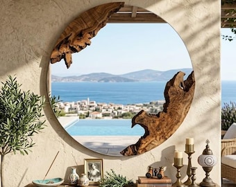 May include: A large circular wall mirror featuring a natural live-edge wood frame with irregular, organic shapes at the top left and bottom right. The reflective surface shows a coastal landscape with a swimming pool, sea, and distant hills.