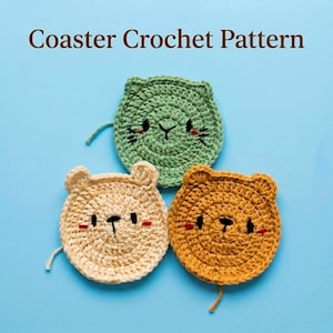 May include: Three circular crochet coasters shaped like animal faces in light green, beige, and mustard yellow. Each coaster features embroidered black eyes, a nose, and small red accents. The text Coaster Crochet Pattern is displayed above.