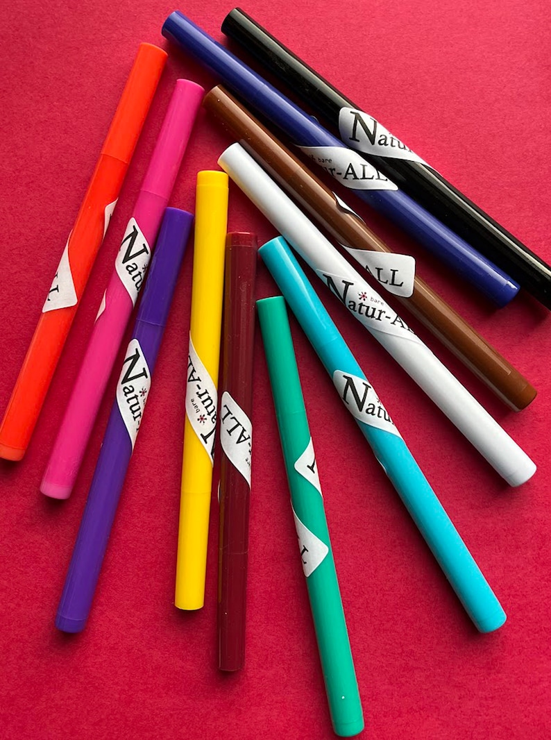 May include: A collection of colorful markers in various shades, including orange, pink, purple, yellow, and blue, arranged on a red surface. Each marker has a white label with the text "Natur-ALL".