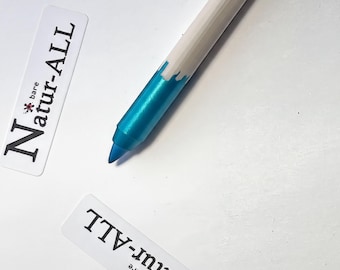 May include: A cosmetic pencil with a white upper body and a metallic turquoise lower section, featuring a pointed blue tip. Two white rectangular labels are present, each printed with the black text Natur-ALL and a small red flower icon.