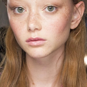 Può includere: Primo piano di una persona con la pelle chiara, lentiggini e capelli castano chiaro. La persona ha occhi verdi, labbra rosa e un leggero rossore sulle guance. I capelli sono divisi a metà e incorniciano il viso.