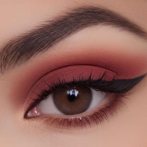 A close-up of an eye with a bold red eye makeup look, featuring a thick black eyeliner wing and a dark brown eye shadow.