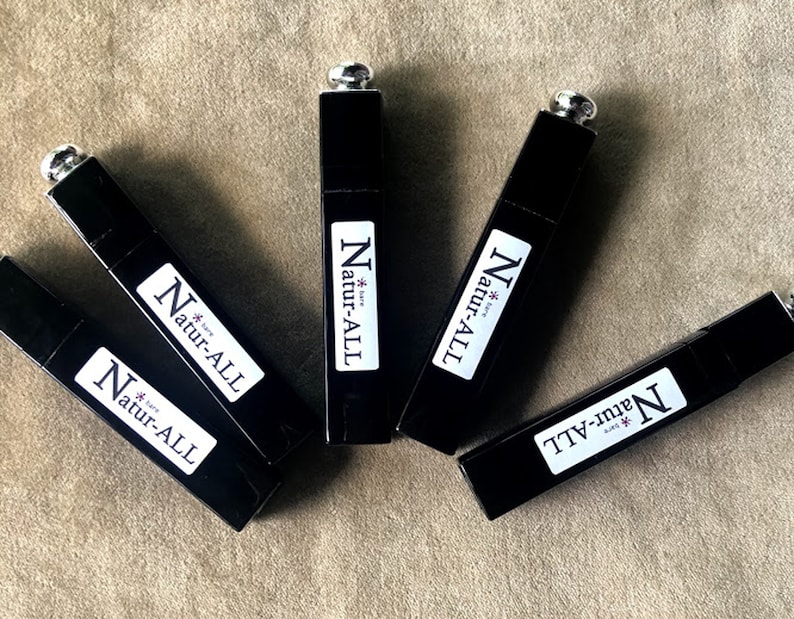 May include: An overhead shot of five black rectangular tubes with silver caps. Each tube has a white label with the text "Natur-ALL" in a bold, sans-serif font. The tubes are arranged on a neutral-toned surface.
