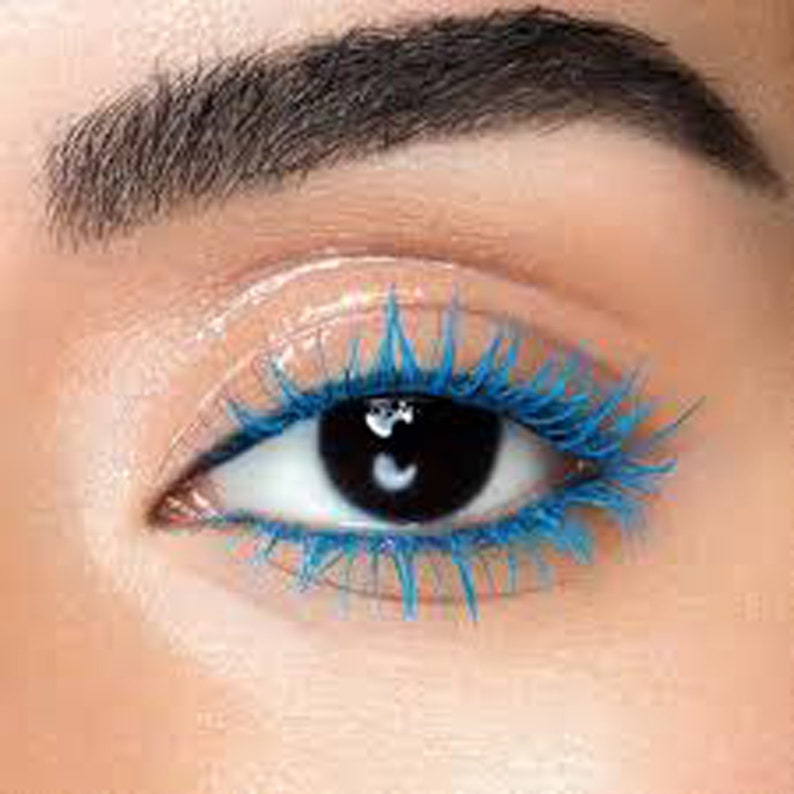 May include: Close-up view of an eye with vibrant blue mascara applied to the upper lashes. The mascara creates a bold, voluminous look with bright blue color. The lashes are long and well-defined, showcasing the mascara's lengthening and volumizing effects.  The eyebrow above is dark and well-groomed. The overall look is dramatic and colorful, ideal for showcasing cosmetic products.