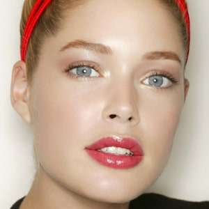 Può includere: Ritratto in primo piano di una persona con la pelle chiara, occhi blu e rossetto rosso. La persona indossa una fascia rossa. La pelle ha un aspetto rugiadoso e illuminato.