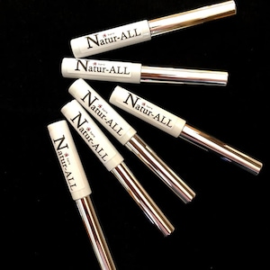 May include: An overhead shot of six Natur-ALL eyeliner pens on a black surface. The pens have white barrels with the brand name printed in black and silver metallic applicators. The pens are arranged in a fan-like pattern.