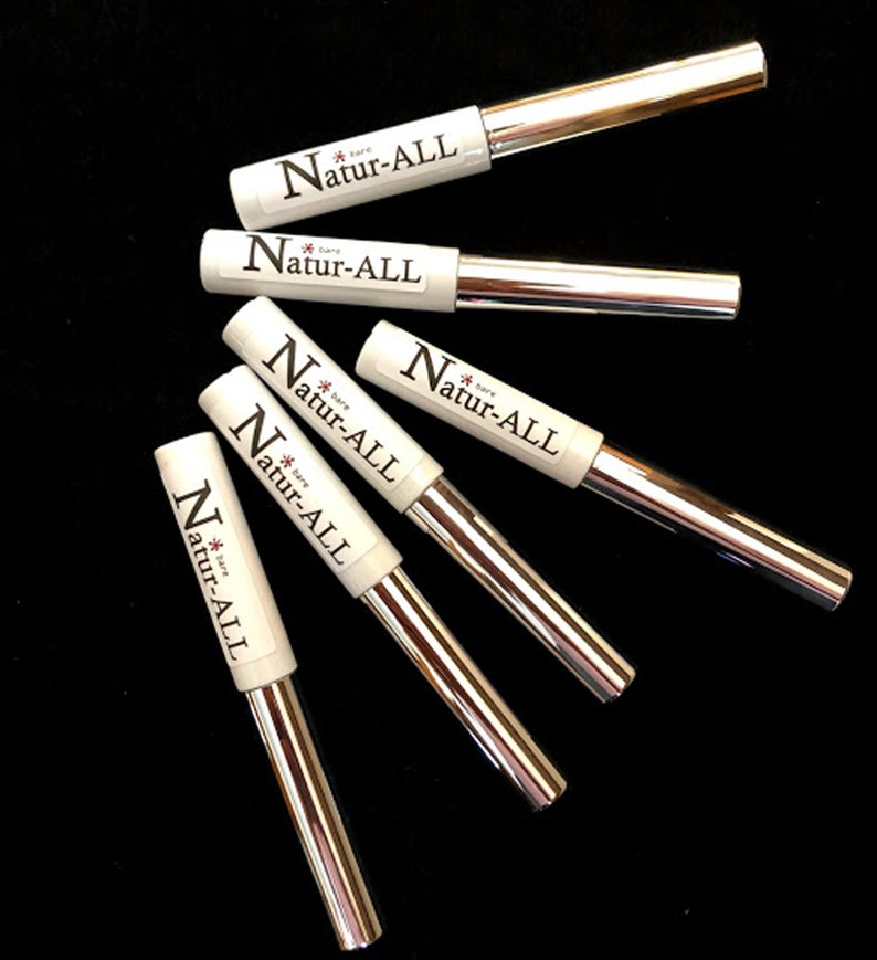 May include: An overhead shot of six Natur-ALL eyeliner pens on a black surface. The pens have white barrels with the brand name printed in black and silver metallic applicators. The pens are arranged in a fan-like pattern.