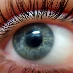 May include: Close-up of a human eye with a blue-green iris. The eye is surrounded by long, dark eyelashes. The image is well-lit, highlighting the details of the eye's texture and the surrounding skin.
