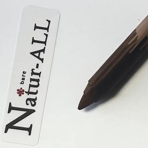 May include: A brown eyeliner pencil next to a white label with the text "bare Natur-ALL" in black and a red flower graphic. The eyeliner pencil has a dark brown tip.