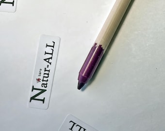 May include: A wooden cosmetic pencil with a light beige casing and a dark purple tip. Next to the pencil is a rectangular white label featuring the text "bare Natur-ALL" in dark green lettering with a small red flower icon above the letter a.