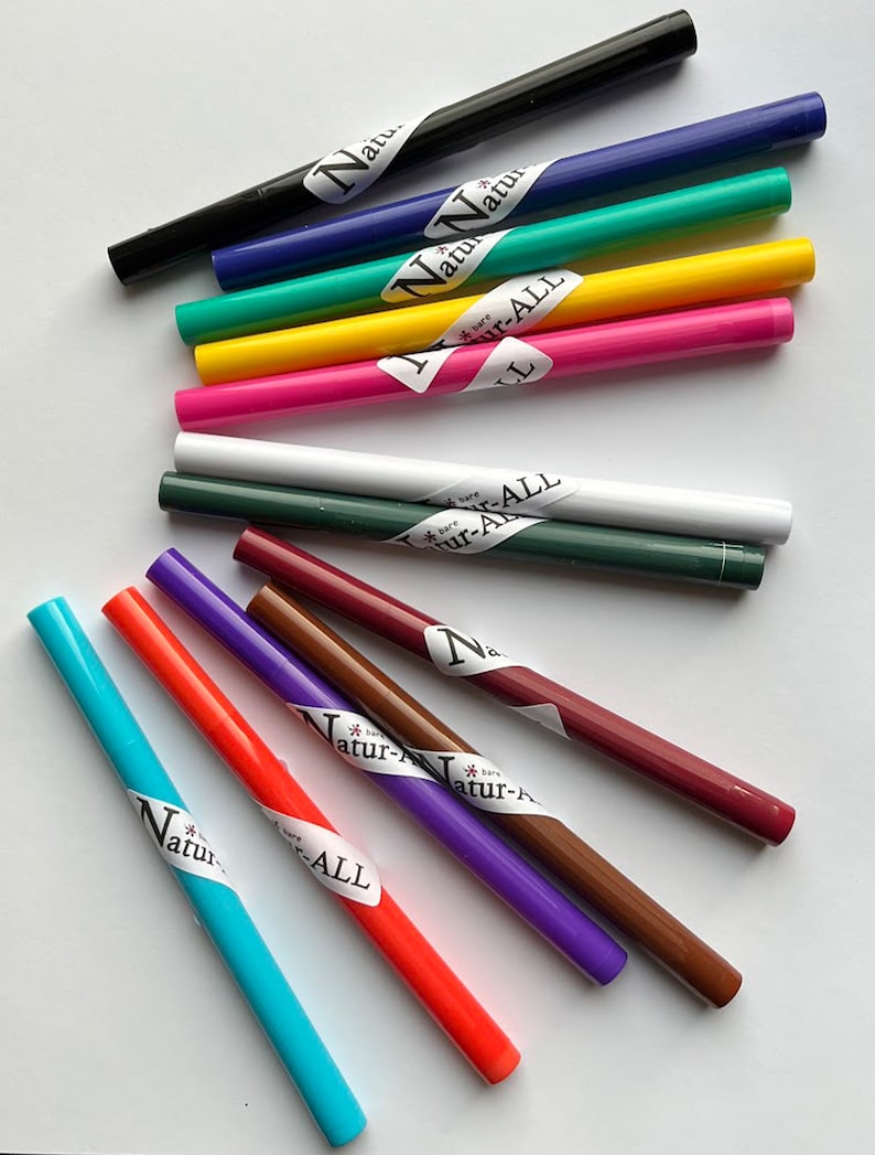 May include: An assortment of colorful eyeliner pencils in various shades, including black, blue, green, yellow, pink, white, and brown. Each pencil has a label with the text "Natur-ALL". The pencils are arranged on a white surface.