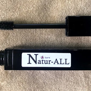 May include: Black mascara tube and wand with the text "bare Natur-ALL". The mascara wand has a black handle and a brush applicator. The mascara tube is black with a white label.