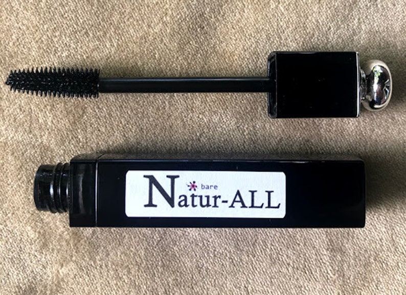 May include: Black mascara tube and wand with the text "bare Natur-ALL". The mascara wand has a black handle and a brush applicator. The mascara tube is black with a white label.