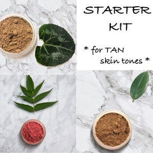 Può includere: Un kit di partenza di bellezza per pelli abbronzate, con due piccoli vasetti di trucco in polvere nelle tonalità marrone e rosa e due foglie verdi. Il testo "STARTER KIT" e "for TAN skin tones" è visualizzato in nero.