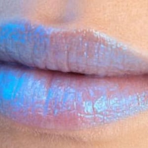 May include: Close-up of lips with iridescent blue lipstick. The glossy lips have a subtle pink undertone, with the blue colour appearing more vibrant in the centre.