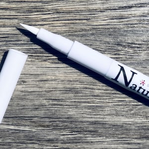 A white marker with the word "Naturals" written on it, lying on a wooden surface.