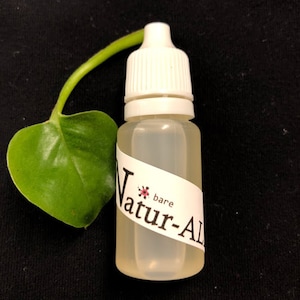May include: A clear plastic bottle with a white cap and a label that reads "Natur-Al". A green leaf and stem are next to the bottle. The background is black.