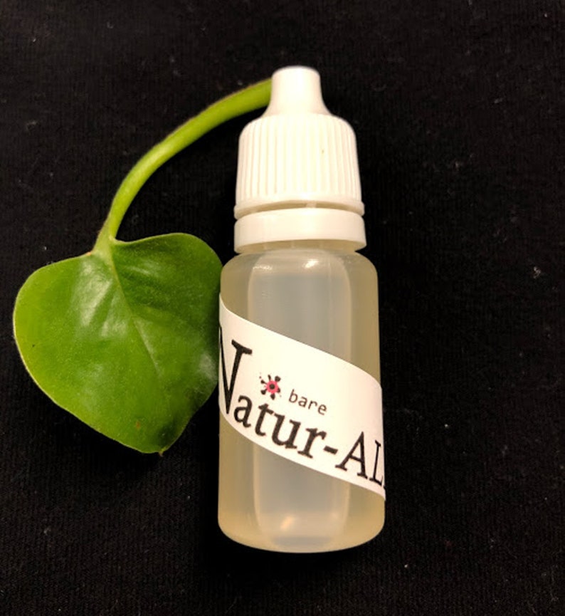 May include: A clear plastic bottle with a white cap and a label that reads "Natur-Al". A green leaf and stem are next to the bottle. The background is black.