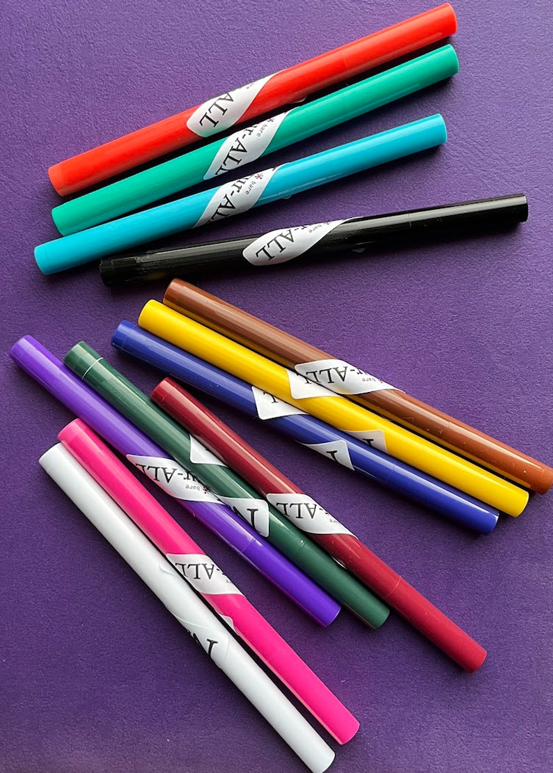 May include: A collection of colorful markers in various shades, including red, green, blue, black, brown, yellow, purple, and pink. Each marker has a white label with the word "ALL" printed on it. The markers are arranged on a purple surface.