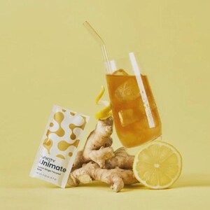 May include: A glass of iced drink with a straw, a packet of Unicity Unimate, ginger root, and a lemon slice, on a yellow background. The Unimate packet has a white and gold design. The ginger and lemon suggest a health drink.