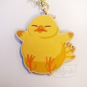May include: A yellow chick keychain with a gold star charm. The chick has closed eyes and a small beak. The keychain is made of wood and has a painted finish.