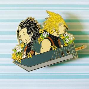 May include: Gold-colored enamel pin featuring two characters from a video game. The characters are standing back-to-back, with one character holding a sword. The characters are surrounded by yellow and white flowers.