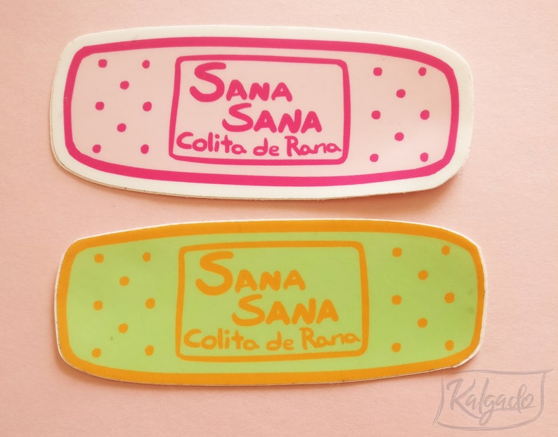 Pode incluir: Dois adesivos coloridos de bandagem com o texto "Sana Sana Colito de Rana" em letras rosa e laranja.