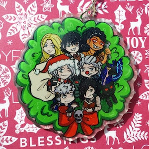 May include: A clear, circular Christmas ornament with cartoon characters inside a green, glittery border. A red bow with a skull is at the bottom. The ornament has a silver-coloured clasp. The background is a festive pink.