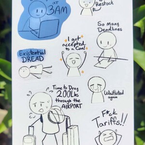 May include: A white sticker sheet featuring humorous illustrations and text. The drawings depict various relatable struggles, including late-night work, deadlines, and travel woes. Text includes "Emailing Manus at 3AM" and "Time to Drag 200Lbs through the AIRPORT."