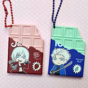 May include: Two novelty chocolate bar keychains. One is pink and red with a cartoon character and strawberry graphic. The other is blue and mint green with a cartoon character and a mint graphic. Both have a bite taken out.