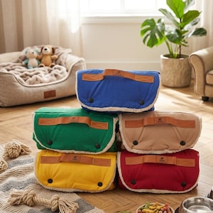 May include: A stack of colorful dog bed covers in blue, green, tan, yellow, and red. Each cover has a brown leather handle and a fluffy white trim. The covers are stacked on a patterned rug.