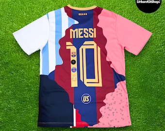 Puede incluir: Una camiseta de fútbol de manga corta con un diseño multicolor que incluye rayas blancas y azul claro, un panel central azul oscuro y granate, y una sección rosa. La espalda muestra el nombre MESSI y el número 10 en dorado con logotipos.