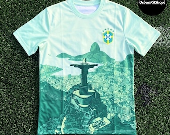 Puede incluir: Una camiseta de manga corta de color verde claro con un estampado gráfico de la estatua del Cristo Redentor sobre Río de Janeiro. El diseño incluye el escudo de la Confederación Brasileña de Fútbol en el pecho y un logotipo circular.