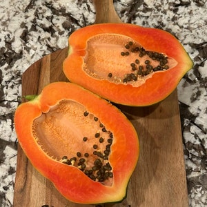 May include: Two halves of a ripe papaya on a wooden cutting board with the words "Slaton Ranch" engraved on the board.