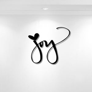 May include: A black wall-mounted sign featuring the word joy written in a flowing, cursive script. The letter j is topped with a small, solid black heart shape, and the final letter y extends into a long, elegant, sweeping curved flourish.