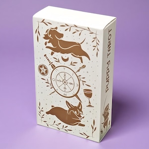 Può includere: Una scatola rettangolare bianca per un mazzo di Puppy Tarot con illustrazioni marroni di due cani, una ruota simile a una bussola, un calice, un pentacolo e stelle. Il lato della scatola mostra il testo Puppy Tarot in un carattere marrone.