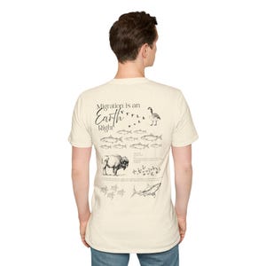 Könnte beinhalten: Ein cremefarbenes Kurzarm-T-Shirt mit einem schwarzen Grafikdruck auf der Rückseite. Das Design zeigt den Text "Migration is an Earth Right" sowie detaillierte Illustrationen einer Gans, verschiedener Fische, eines Bisons und eines Hais.