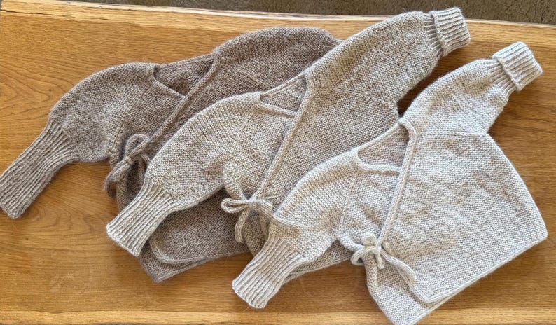 May include: Three long-sleeved wrap-style cardigans in varying shades of beige, tan, and light brown. Each garment features a knitted texture, ribbed cuffs at the wrists, and a side-tie closure with matching knitted strings to secure the front overlap.