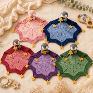 May include: Five handmade crochet baby security blankets in pink, blue, red, purple, and green. Each blanket features a star-shaped design, yellow star accents, and a small penguin toy holding a yellow star. A wooden baby rattle is also visible.