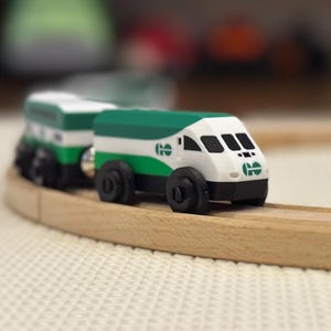 May include: A toy train set with a white and green train car on a wooden track. The train car has the letters "GO" on the side. The track is on a white surface. The train is travelling on a wooden track.