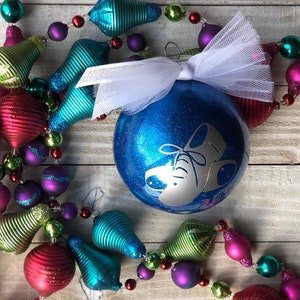 May include: A blue glitter Christmas ornament with a white design of a pair of ice skates. The ornament is decorated with a white tulle bow and is surrounded by a garland of colorful ornaments.