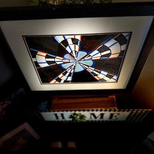 May include: Framed abstract art with a black frame and white mat. The artwork features a radial design with black, white, red, and blue segments on a dark background. Decorative home decor.
