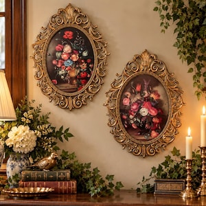 May include: Two oval wall art pieces featuring floral still life paintings in ornate gold frames. Each frame has intricate scrollwork and leaf detailing. The paintings depict colorful bouquets of flowers against dark backgrounds.