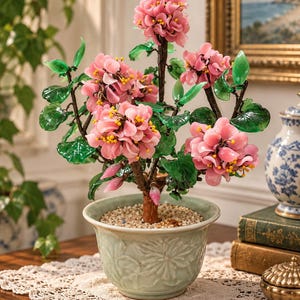 May include: A decorative bonsai-style tree featuring clusters of pink translucent flower petals with yellow centers and green leaves. The tree has a brown trunk and is planted in a light green ceramic pot with a floral relief pattern.