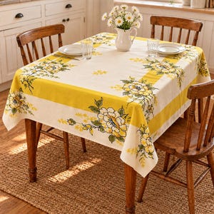 May include: A rectangular tablecloth featuring a cream-colored center and wide yellow borders, decorated with a floral pattern of yellow and white flowers with green leaves. The cloth is draped over a wooden table with four chairs.