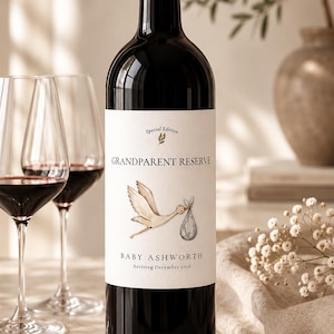 Peut inclure: Une bouteille de vin en verre foncé avec une étiquette blanche illustrée d'une cigogne portant un baluchon. Le texte indique Special Edition, GRANDPARENT RESERVE, BABY ASHWORTH et Arriving December 2026. La bouteille a un bouchon noir.